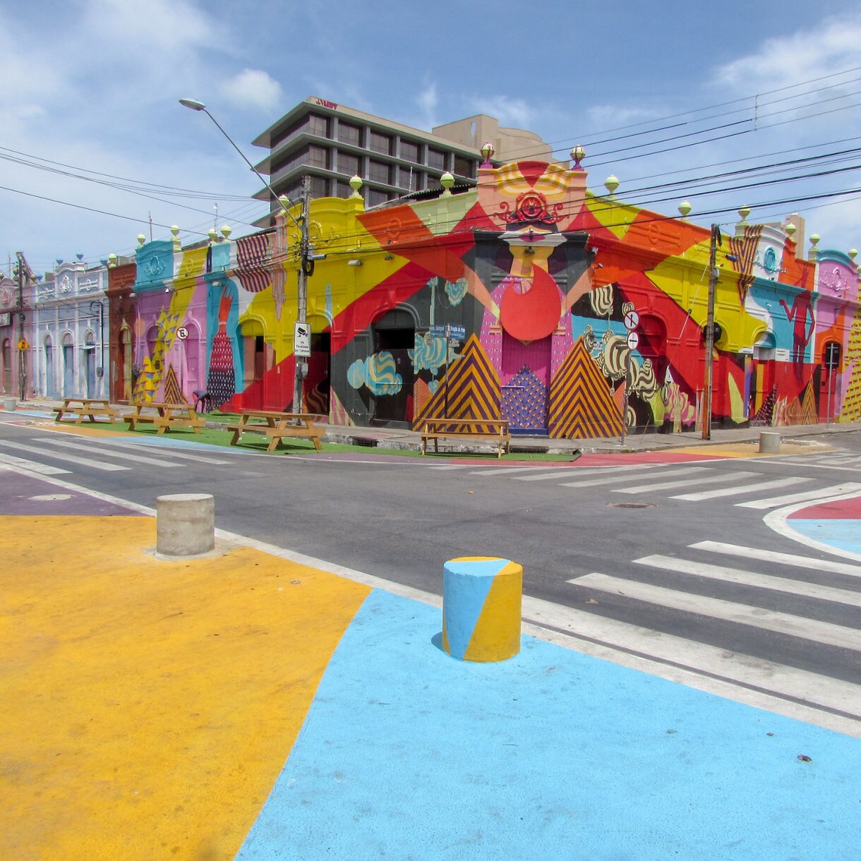 Row of historic colonial buildings covered in bright, multicolored murals along a quiet street with painted sidewalks and pedestrian areas in Fortaleza’s port district.