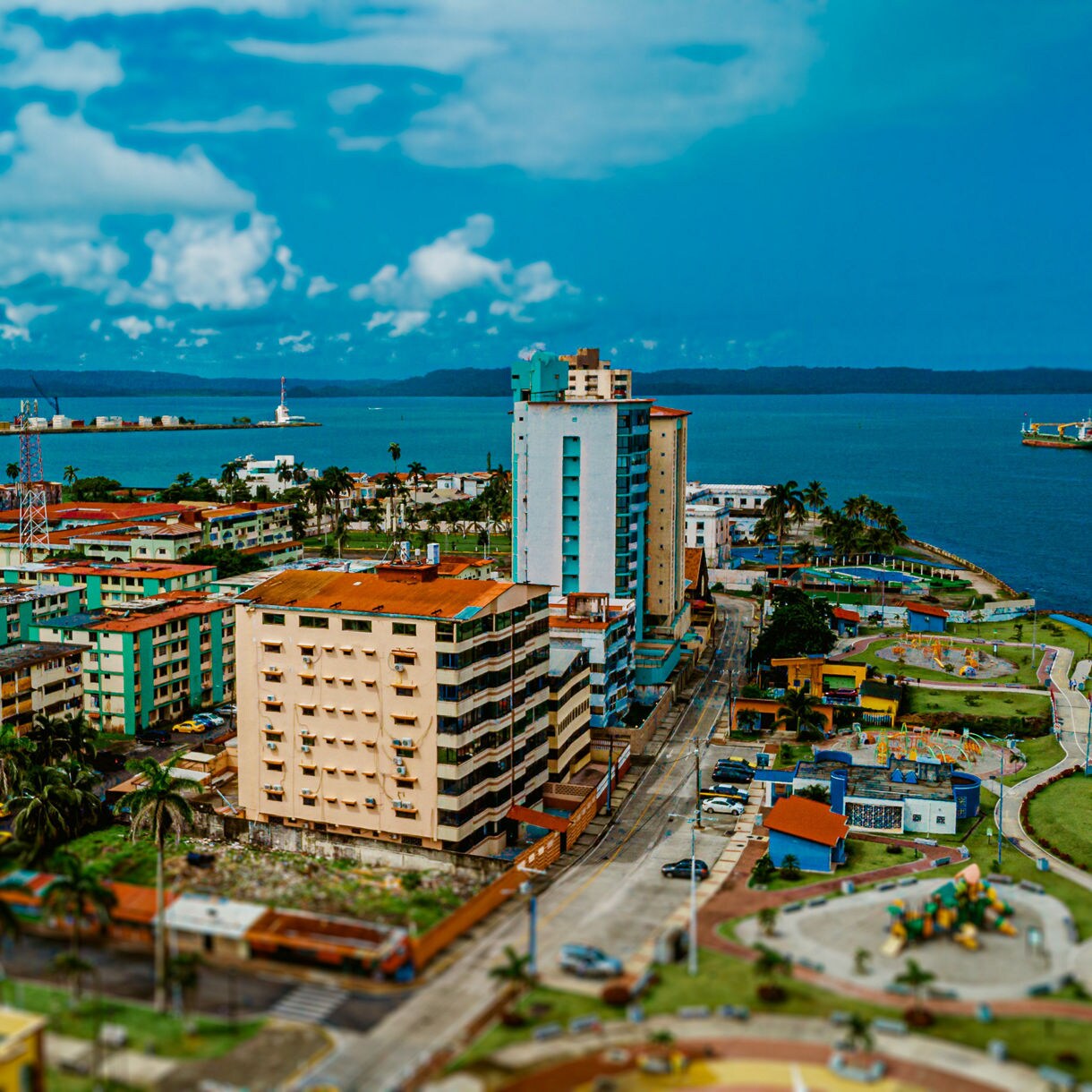 Aerial view of Colón, Panama, showing pastel-colored buildings, palm-lined streets and the coastline with ships docked offshore.