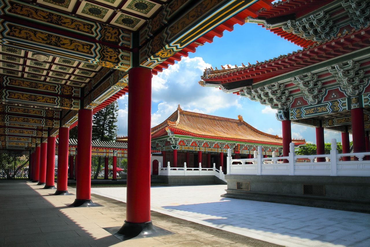 The richly decorated halls of the Confucius Temple in Kaohsiung, Taiwan, featuring red columns, intricate painted ceilings and golden-tiled roofs under a bright sky.