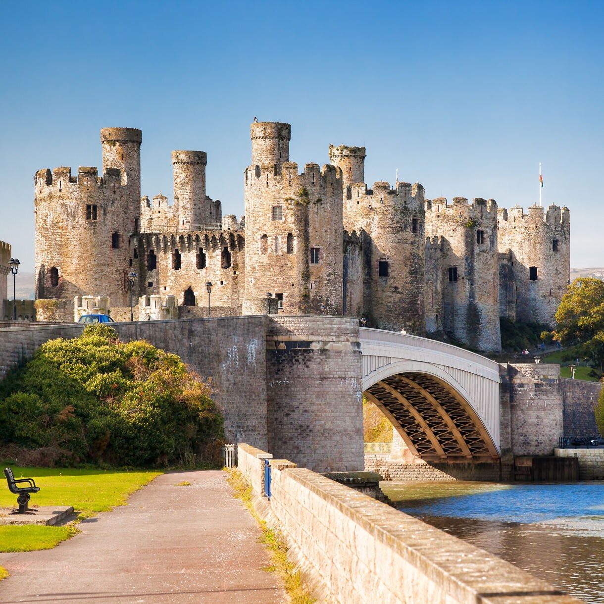 Conwy Castle in Wales with its tall round towers and stone walls overlooking a bridge and river with a sailboat.