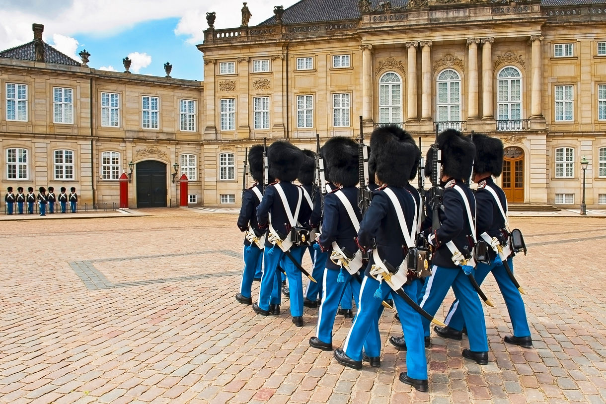 Danish royal guards in blue uniforms and tall bearskin hats performing a ceremonial march at Amalienborg Palace.