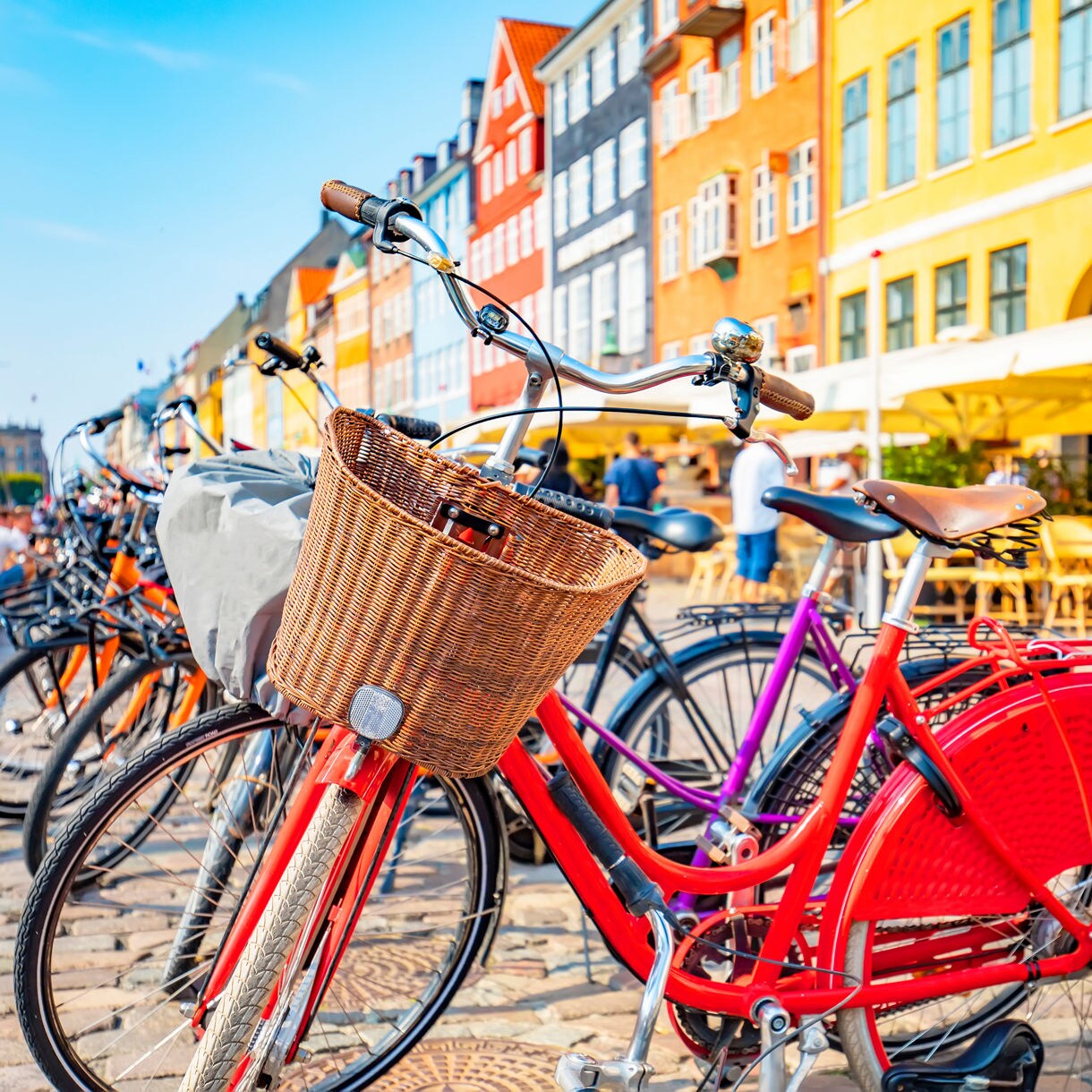 Row of bicycles with a red bike in front, set against bright buildings and outdoor cafés in Nyhavn, Copenhagen.