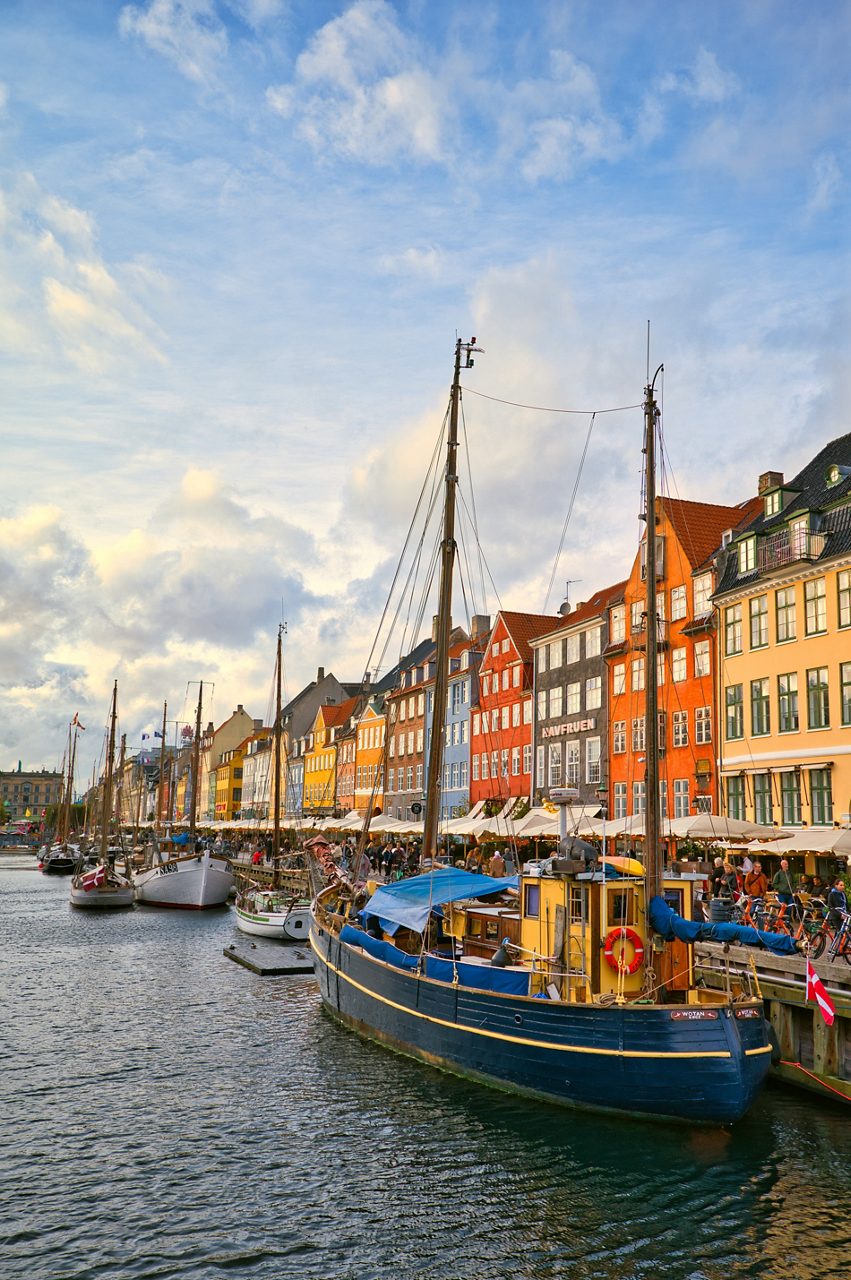 Colorful Nyhavn buildings with docked wooden boats lining the canal at sunset in Copenhagen.
