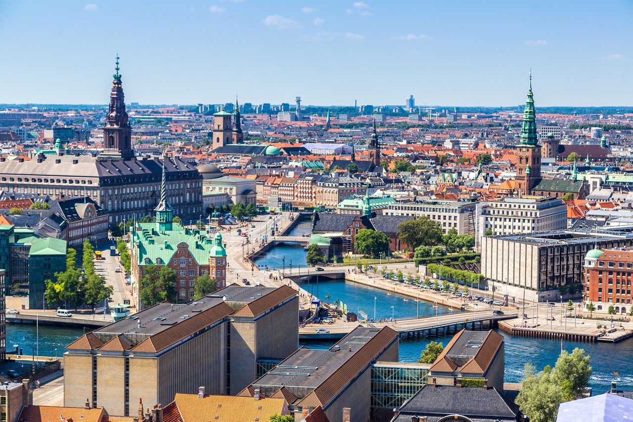 Aerial view of Copenhagen with waterways, historic towers, and colorful rooftops under a clear sky.