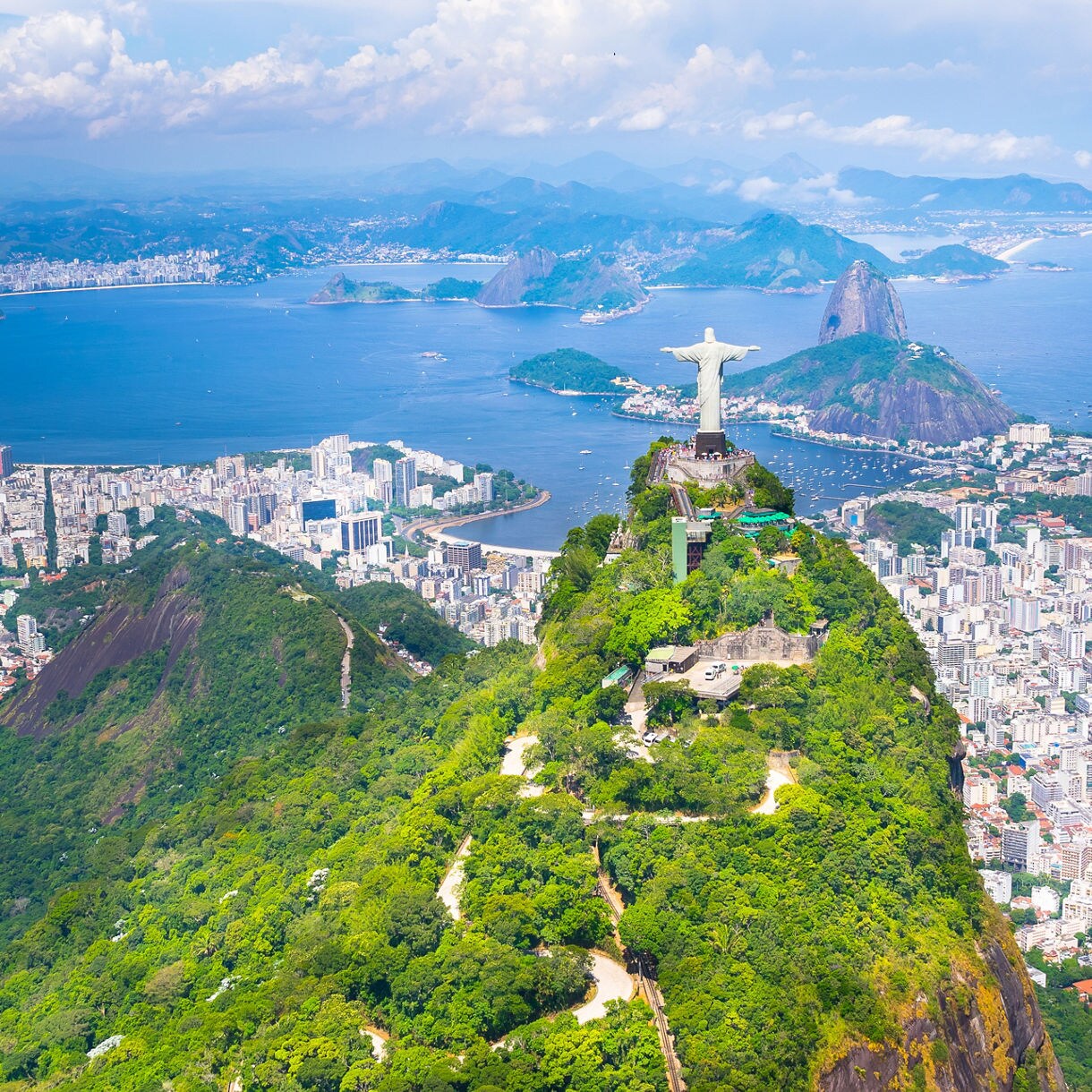 Aerial view of Corcovado Mountain with the Christ the Redeemer statue overlooking Rio de Janeiro’s cityscape, green hills and blue coastal waters.