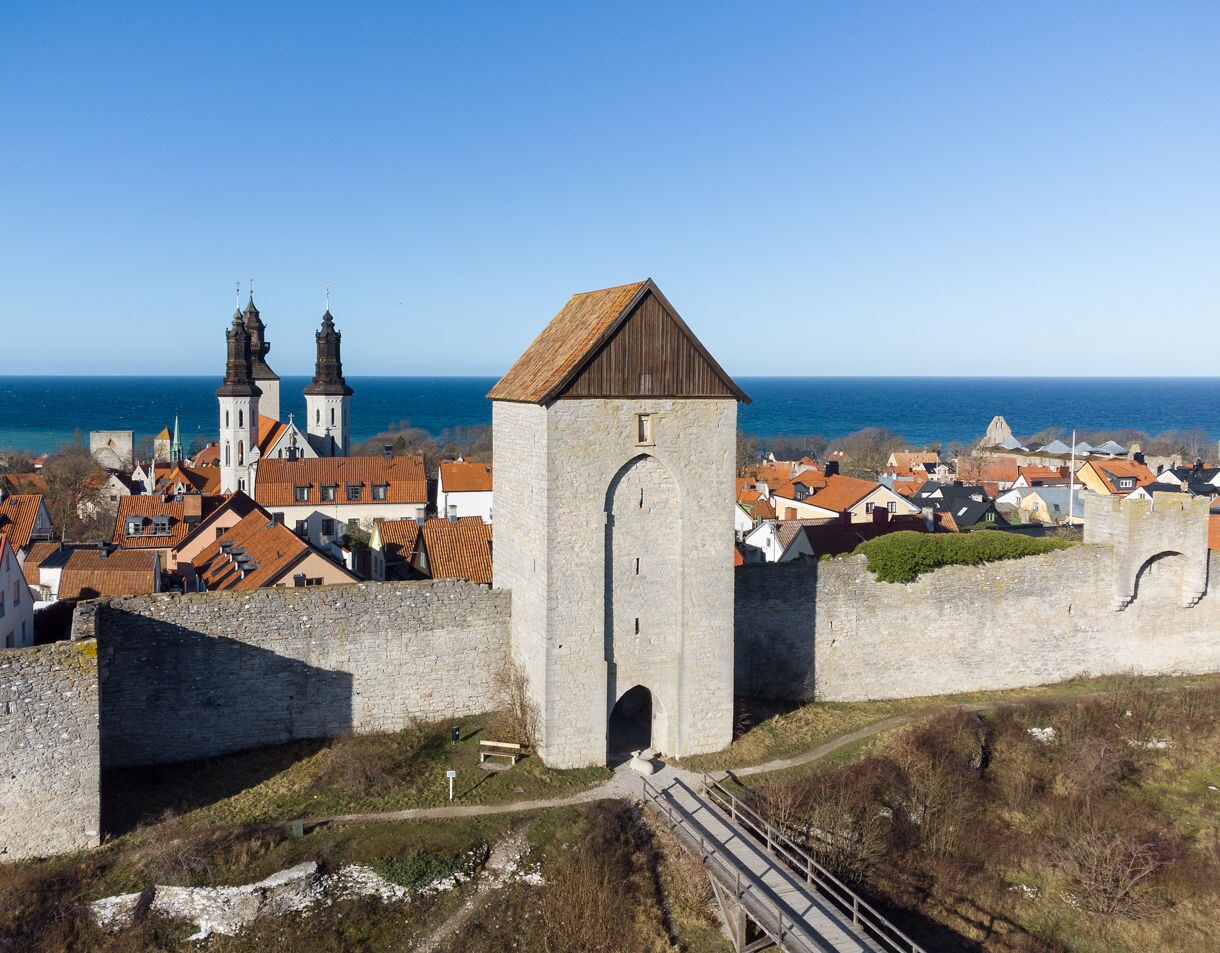 Aerial view of Visby’s city wall and Dalmansporten gate with church towers and the Baltic Sea in the background.