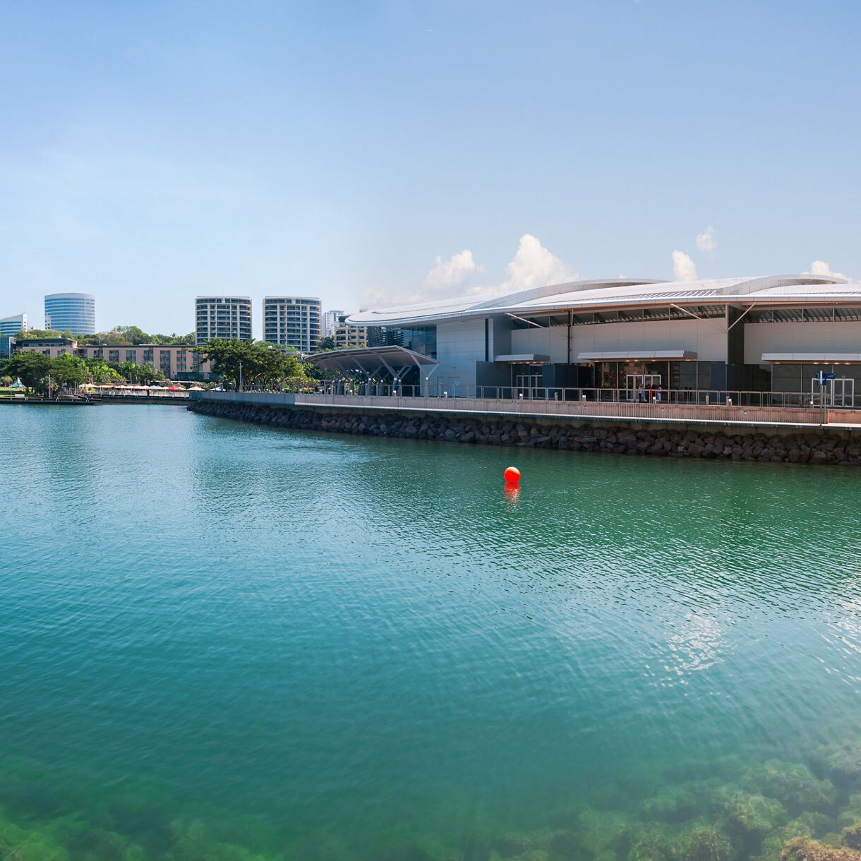 Scenic view of the Darwin Waterfront with modern apartments, clear blue water and a waterfront promenade under a sunny sky.