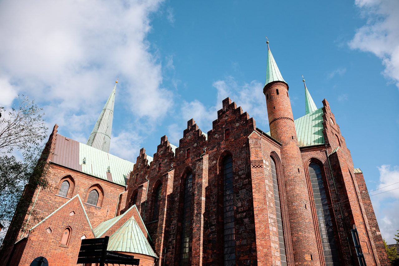 Close-up of Aarhus Cathedral’s Gothic brick exterior with tall arched windows and copper spires under blue sky.