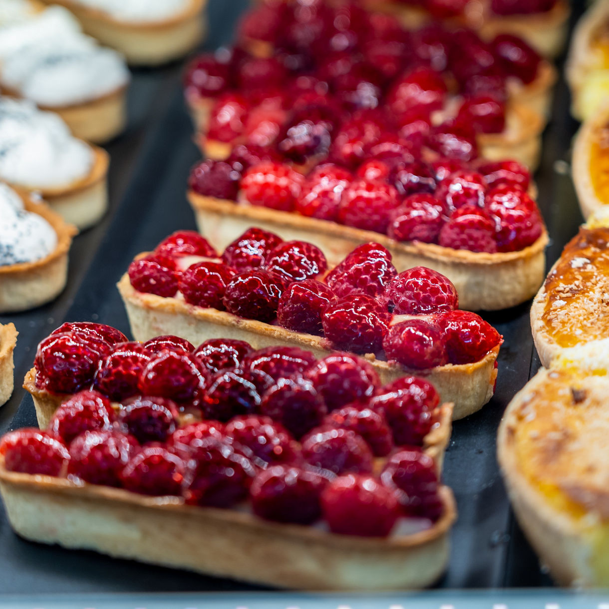 Display of raspberry tarts beside lemon tarts topped with poppy seed cream in golden pastry shells.
