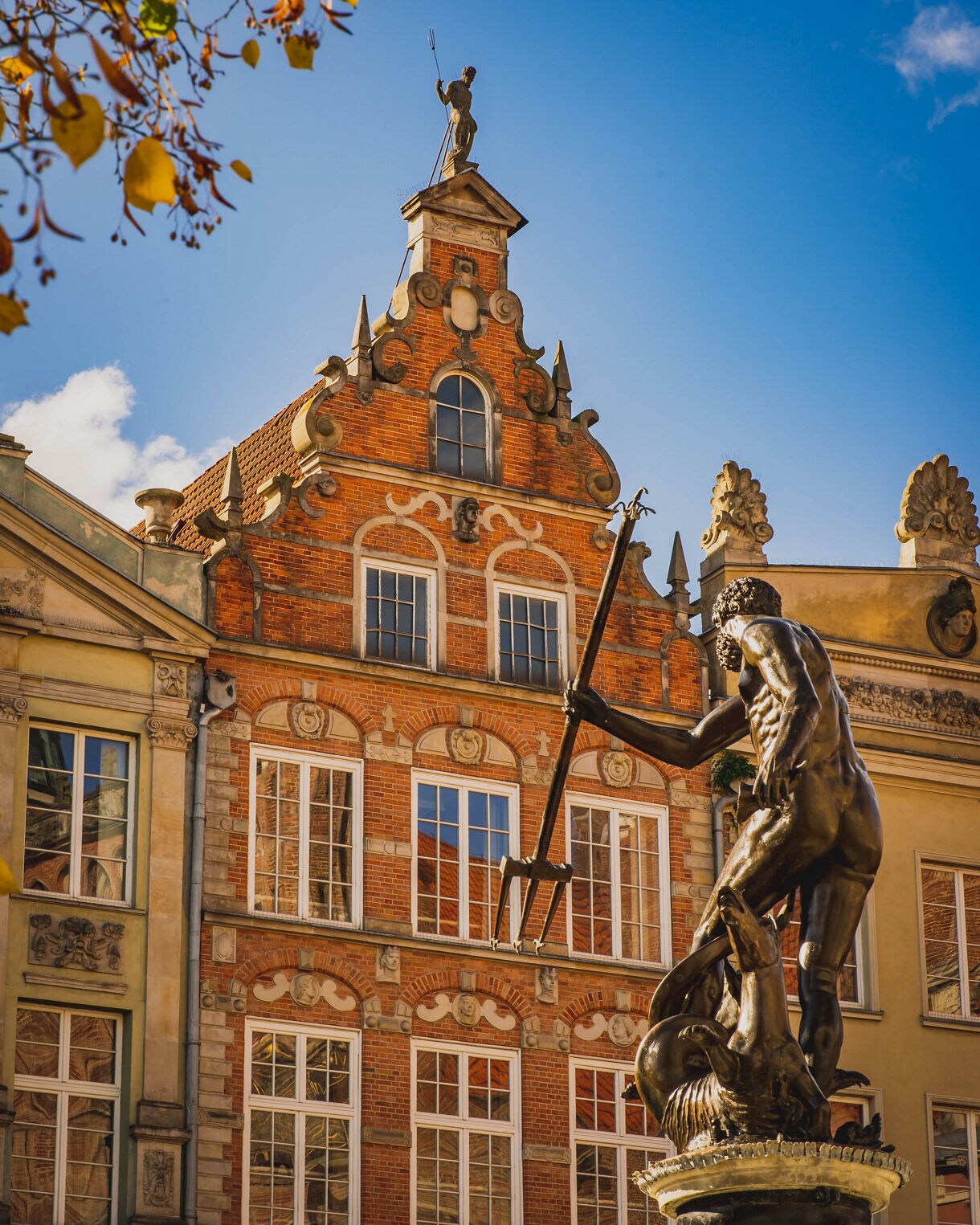Bronze Neptune Fountain statue with trident in Gdańsk’s Długi Targ square, set against ornate brick and stone façades.