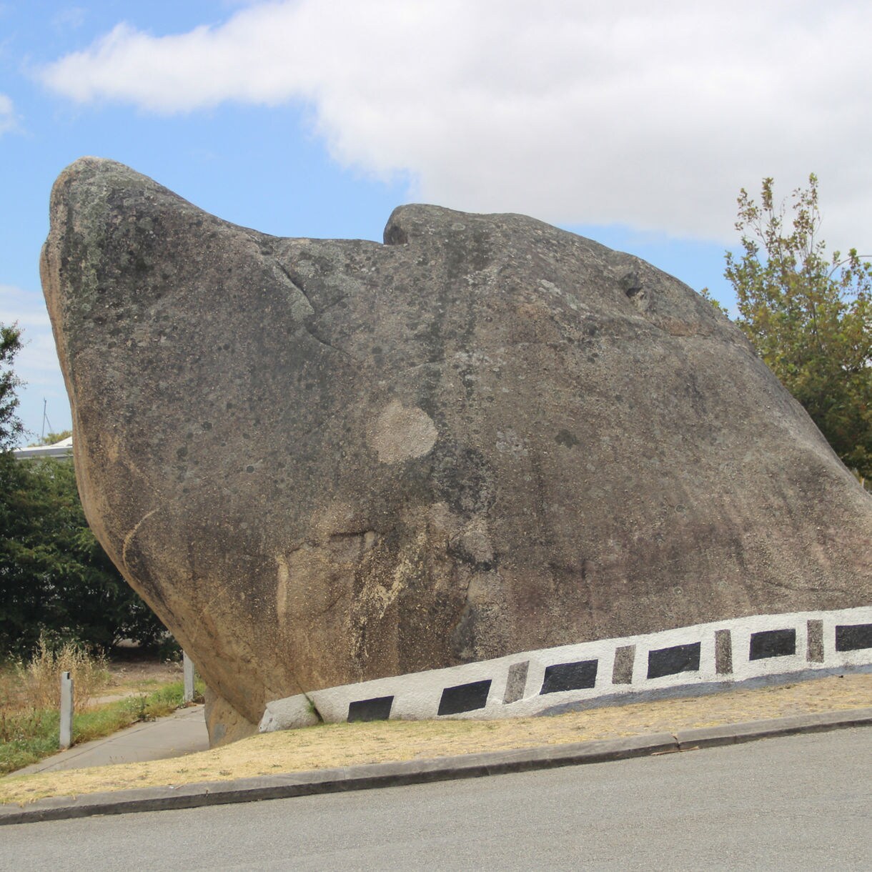 Large granite rock beside a road shaped like a dog’s head, with painted markings near the base.