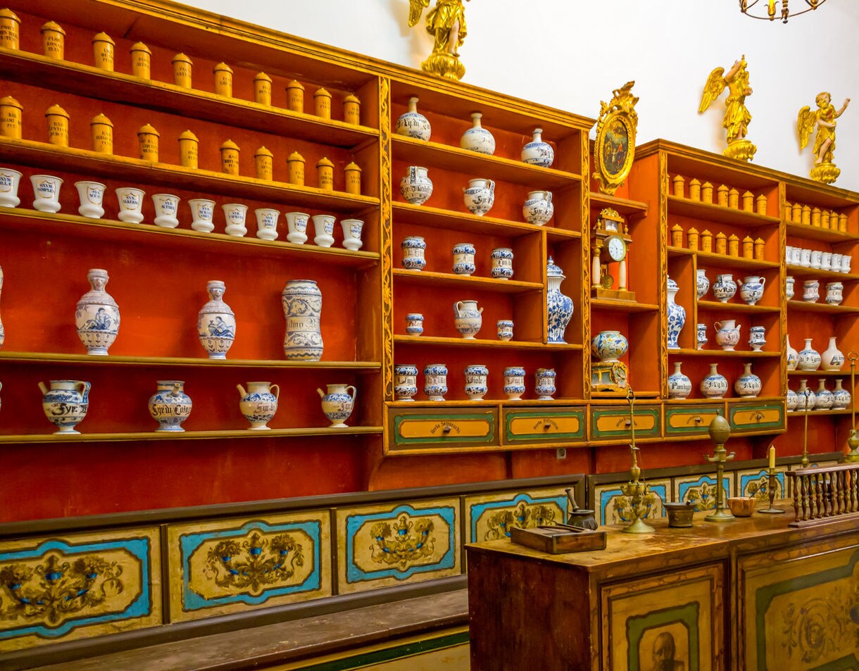 Historic pharmacy interior in Dubrovnik, featuring wooden shelves with ornate jars, ceramic containers and antique tools.