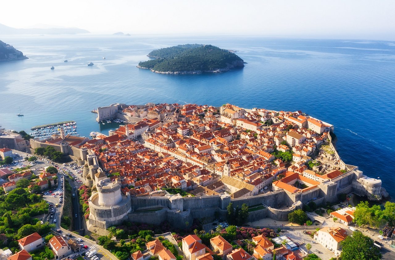 Aerial view of Dubrovnik, Croatia, showing the walled old town with terracotta rooftops, fortifications and nearby Lokrum Island surrounded by deep blue sea.