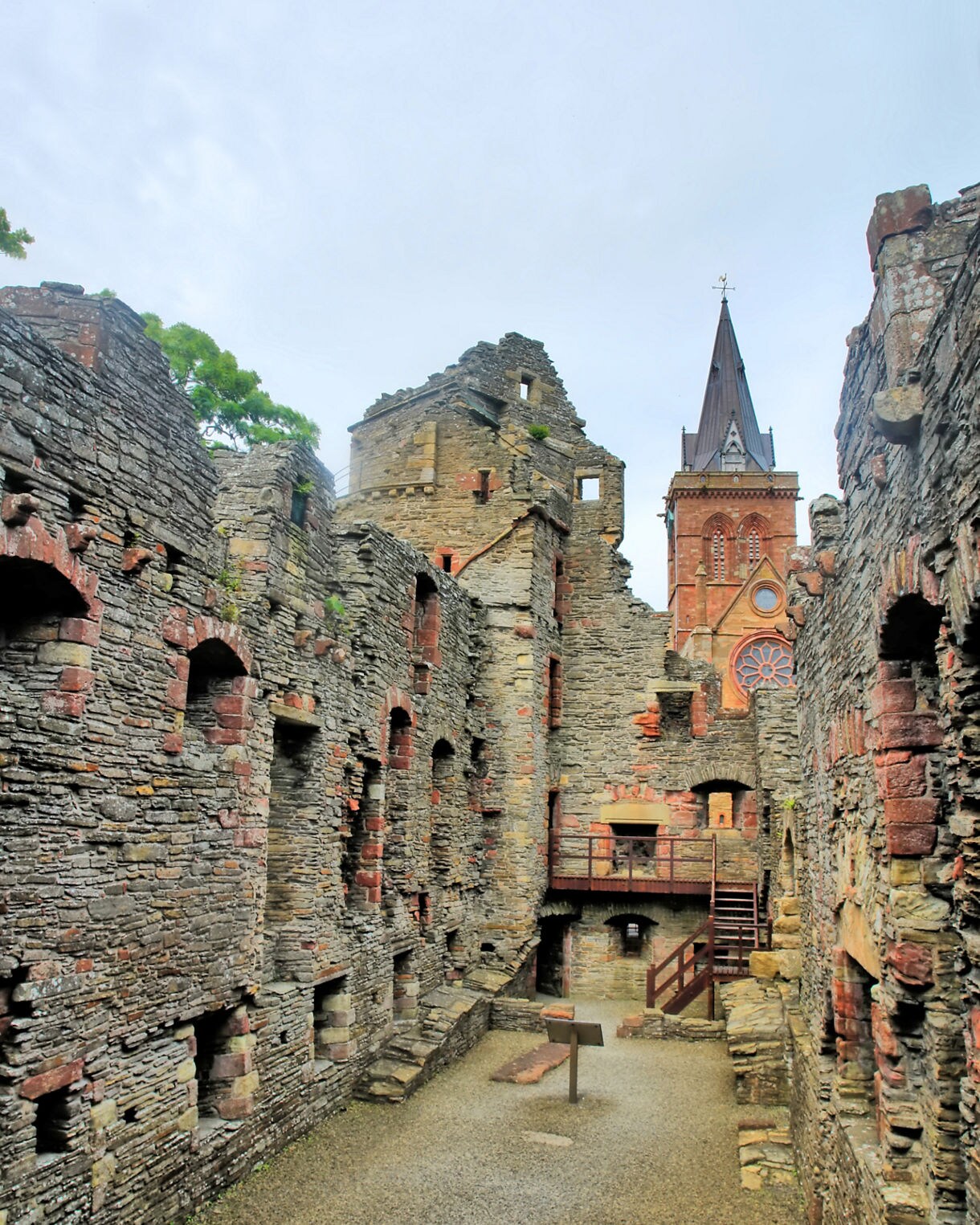 Stone ruins of the Earl’s Palace in Kirkwall, showing weathered walls, arched windows and St Magnus Cathedral’s spire in the background.