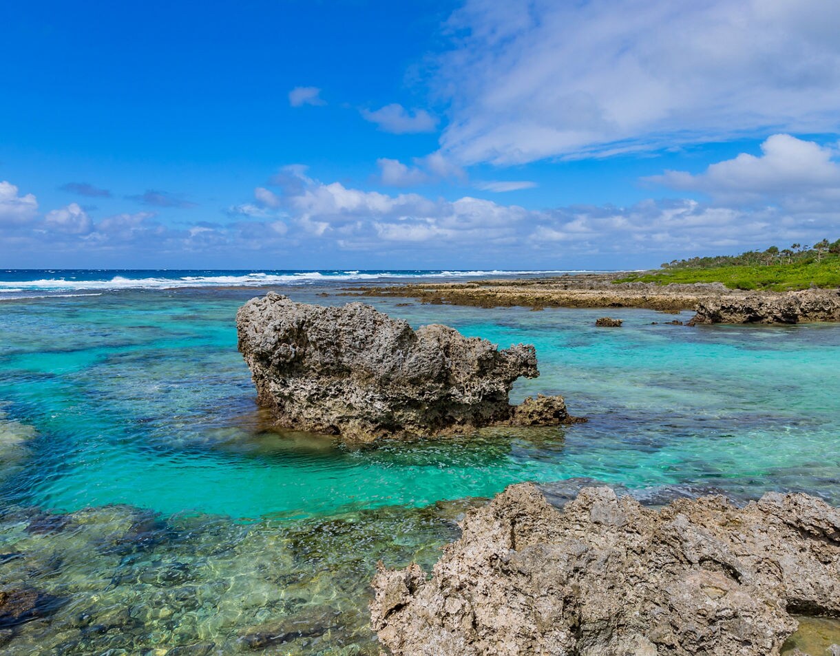 Coral rock formations rising from shallow turquoise water along Efate Island’s rugged coast under a bright blue sky.