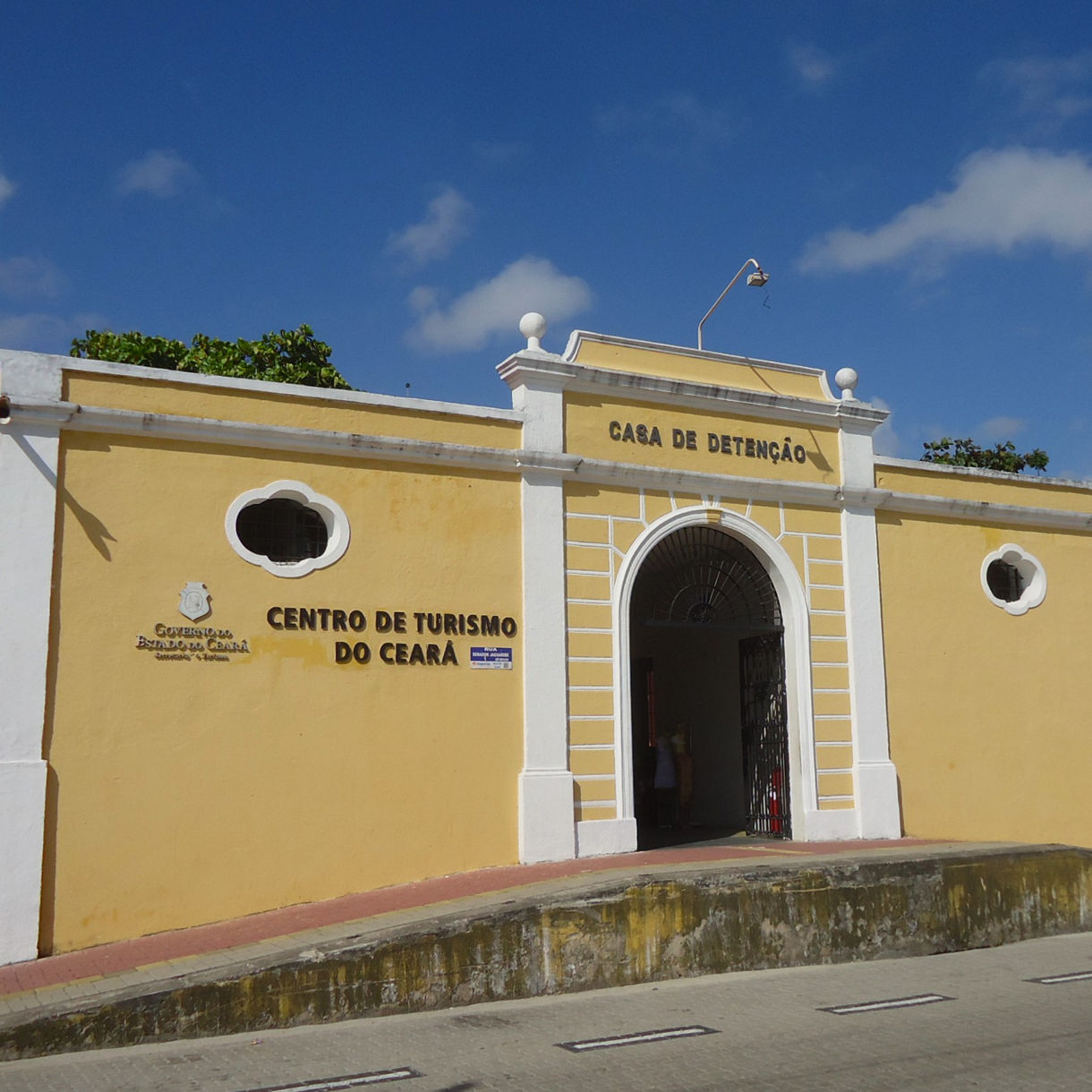 Yellow colonial-style building with white trim, arched entrance and small oval windows, marked as the Ceará Tourism Center.
