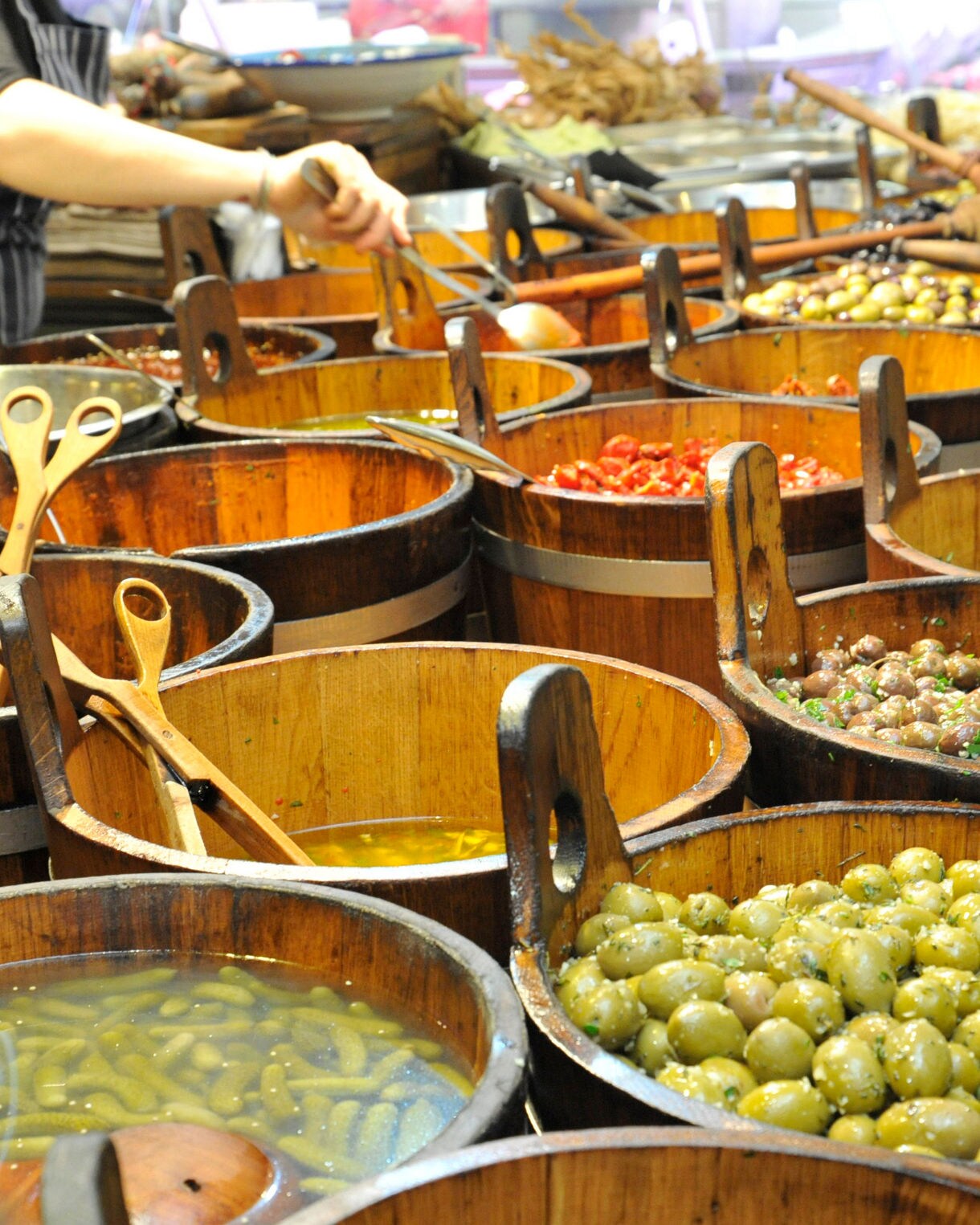 Wooden barrels filled with assorted olives, pickles and marinated vegetables at the English Market in Cork, with wooden ladles resting inside each container.