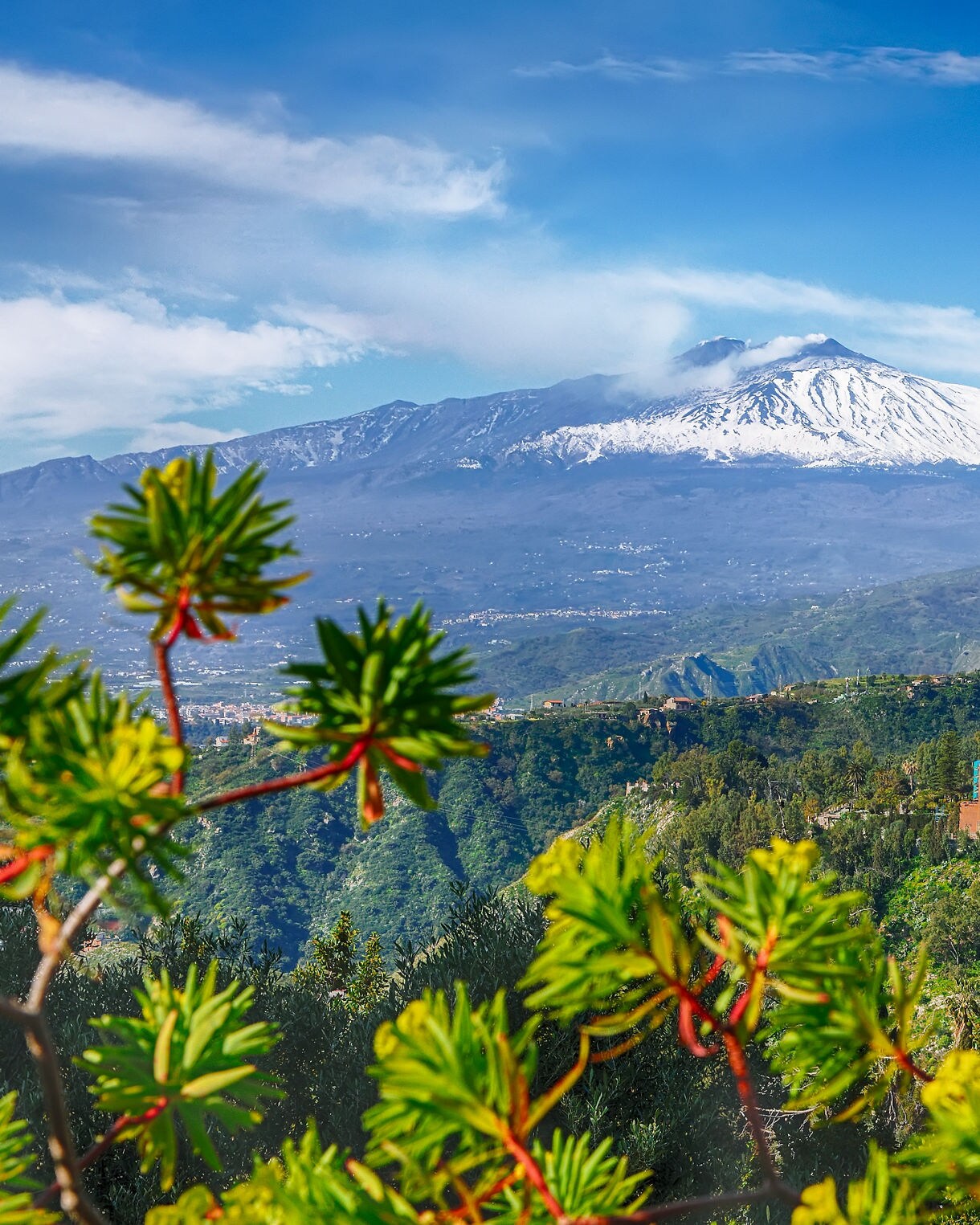 Colorful hillside town of Taormina with Mount Etna’s snowy peak in the distance under a clear blue sky.