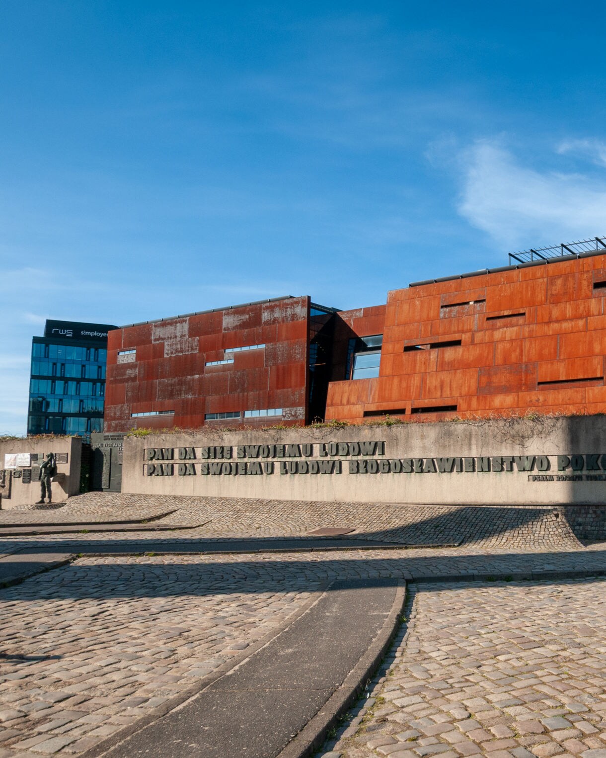 Modern rust-colored European Solidarity Centre building in Gdańsk, Poland, with industrial-style design and engraved concrete wall in the foreground.