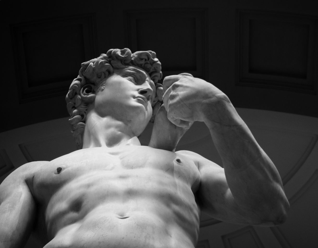 Close-up view of Michelangelo’s marble David statue, showing the upper torso, curled hair and clenched hand, captured from a low angle inside a domed gallery.