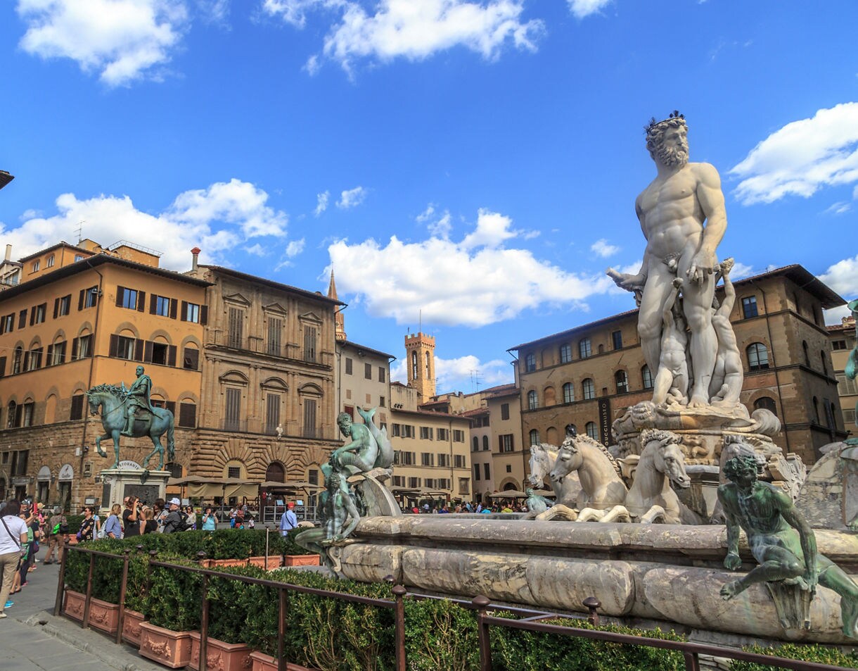 A bustling city square in Florence featuring the Fountain of Neptune with its marble figures and bronze statues, surrounded by historic stone buildings and crowds of people enjoying the open plaza