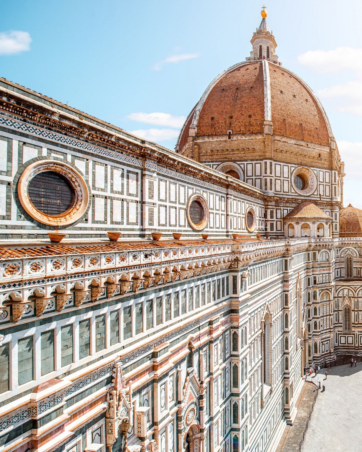 View of the Florence Cathedral with its large brick dome and patterned marble exterior overlooking a sunlit city square.
