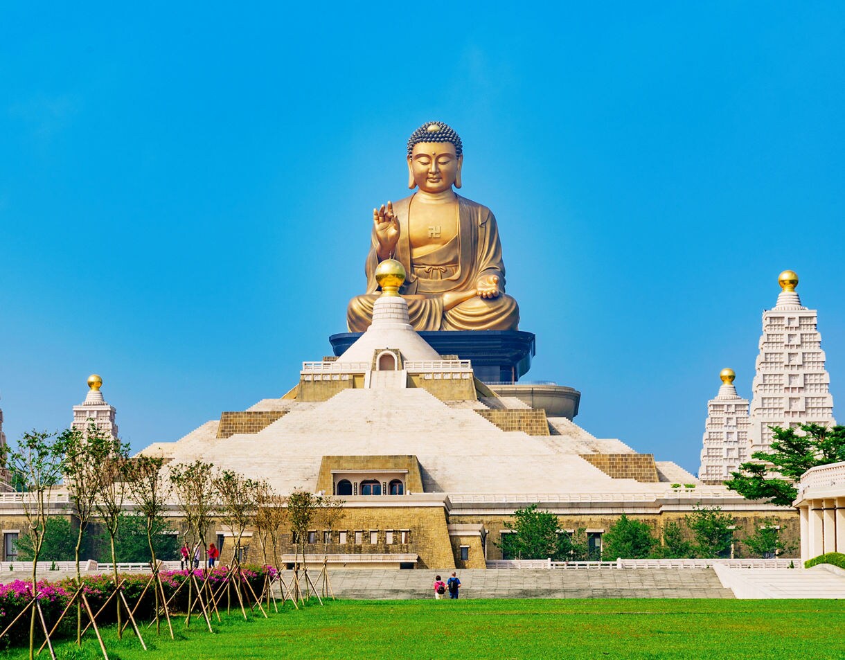 The massive golden Buddha statue at Fo Guang Shan Monastery in Kaohsiung, Taiwan, surrounded by symmetrical pagodas and lush green gardens under a bright blue sky