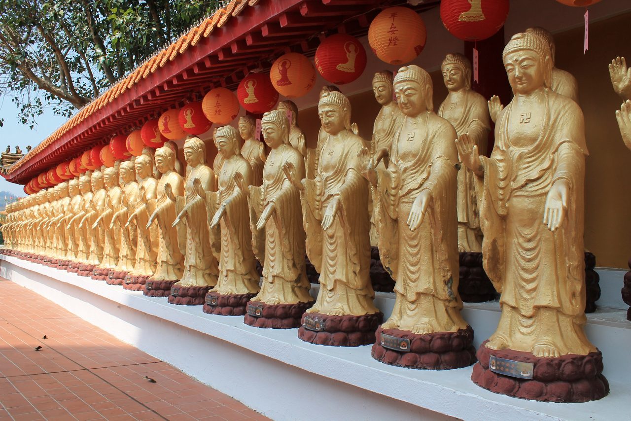 Dozens of golden Buddha statues lined beneath red lanterns at Fo Guang Shan Monastery in Kaohsiung, Taiwan.