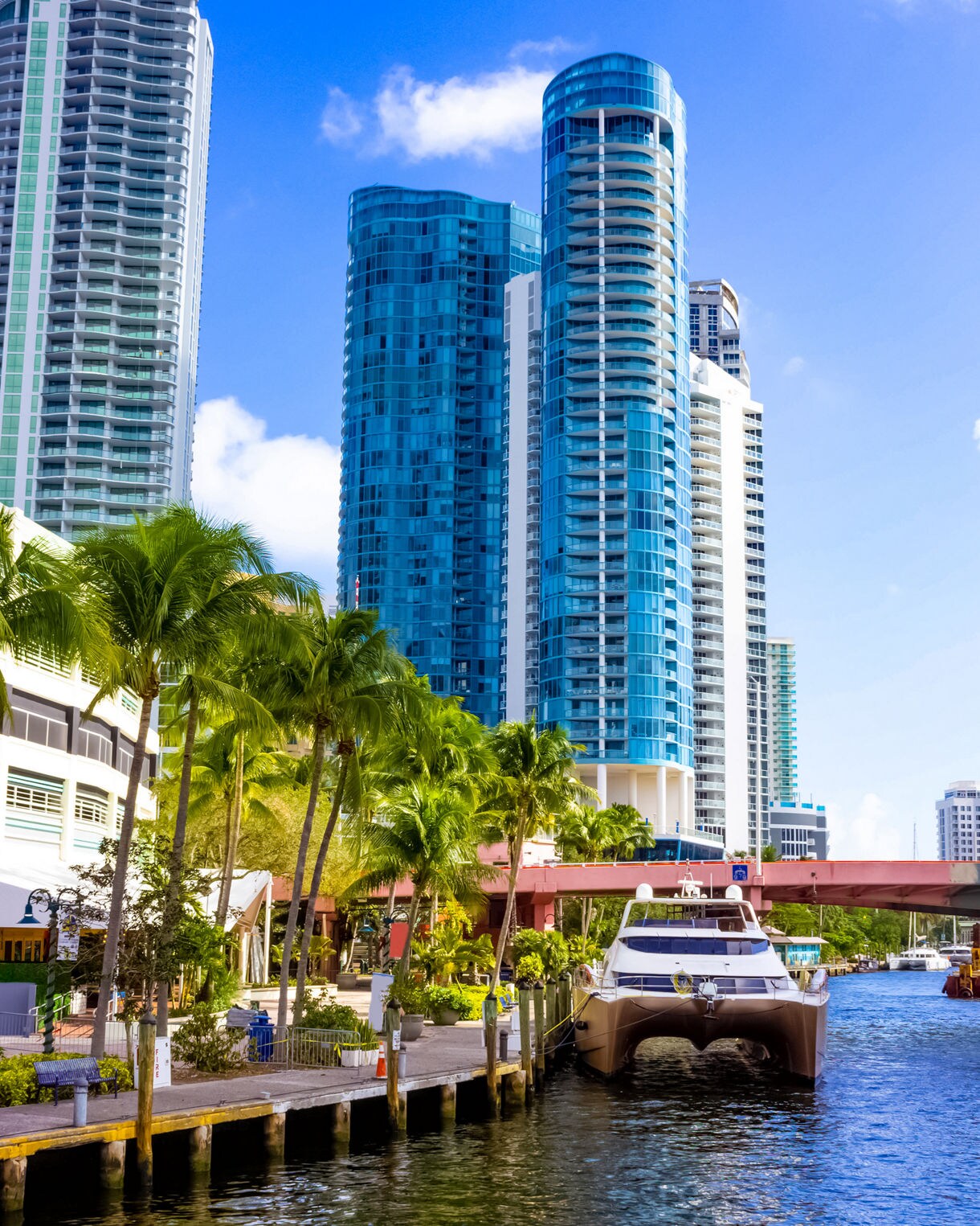 Tall glass skyscrapers rising above palm-lined docks in Fort Lauderdale with a yacht moored by the water.