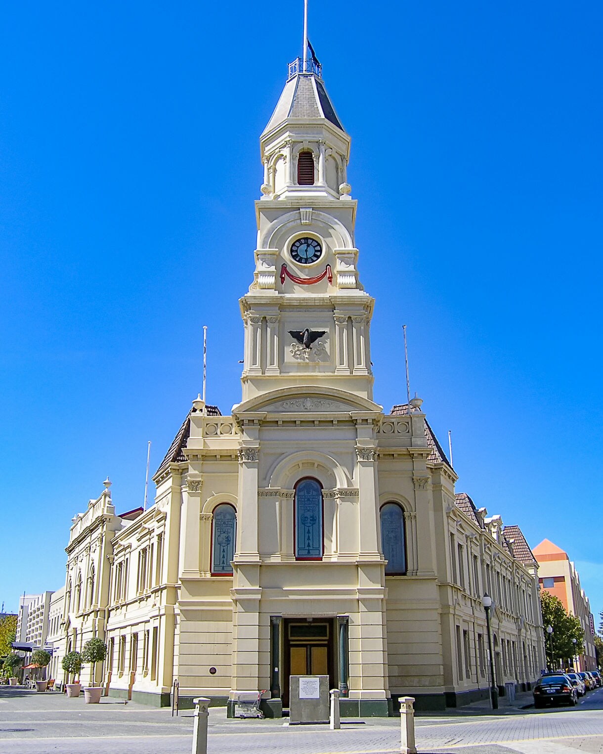 Historic Fremantle Town Hall with a tall clock tower, cream-colored façade and arched windows under a clear blue sky.