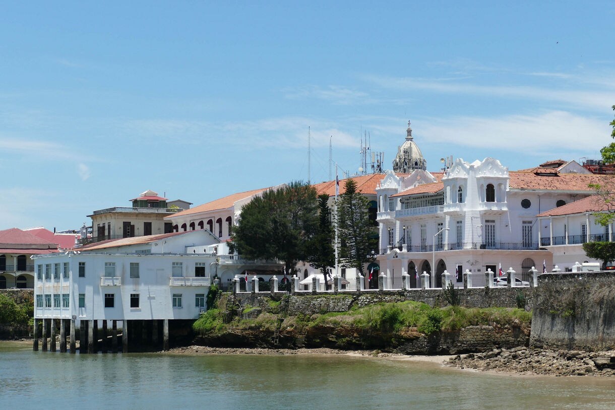 Coastal view of Casco Viejo with white and pastel colonial buildings, red tile rooftops and a domed structure rising above the skyline.