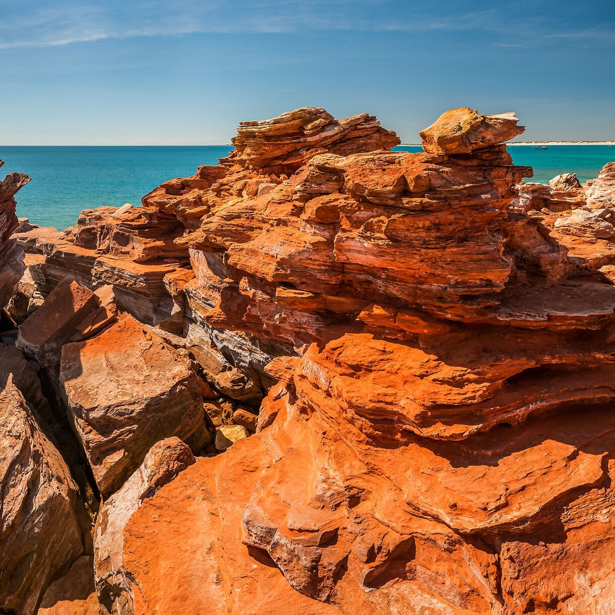 Jagged red sandstone cliffs beside clear turquoise water under a bright blue sky.