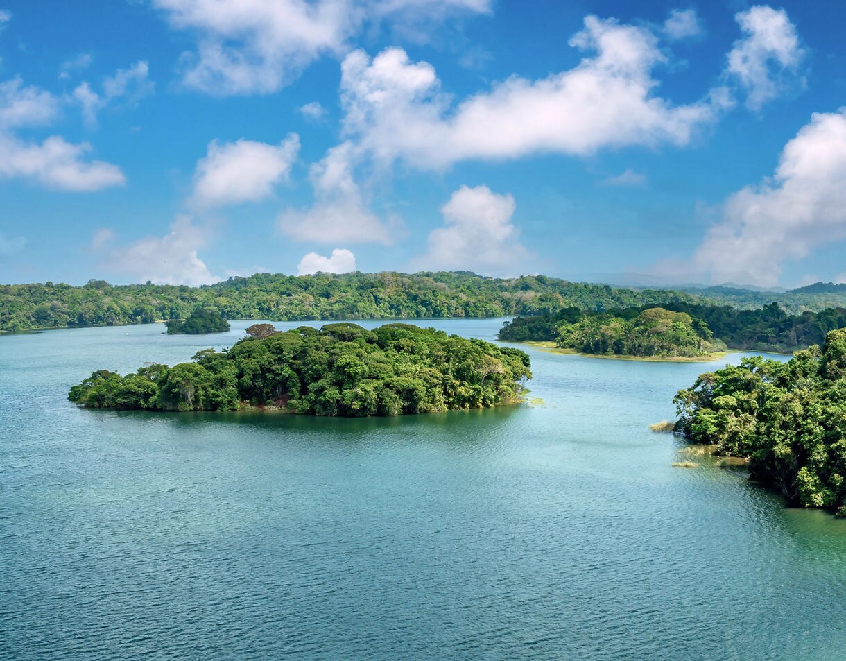 Green tropical islands surrounded by blue waters of Gatun Lake in Panama under a bright, partly cloudy sky.