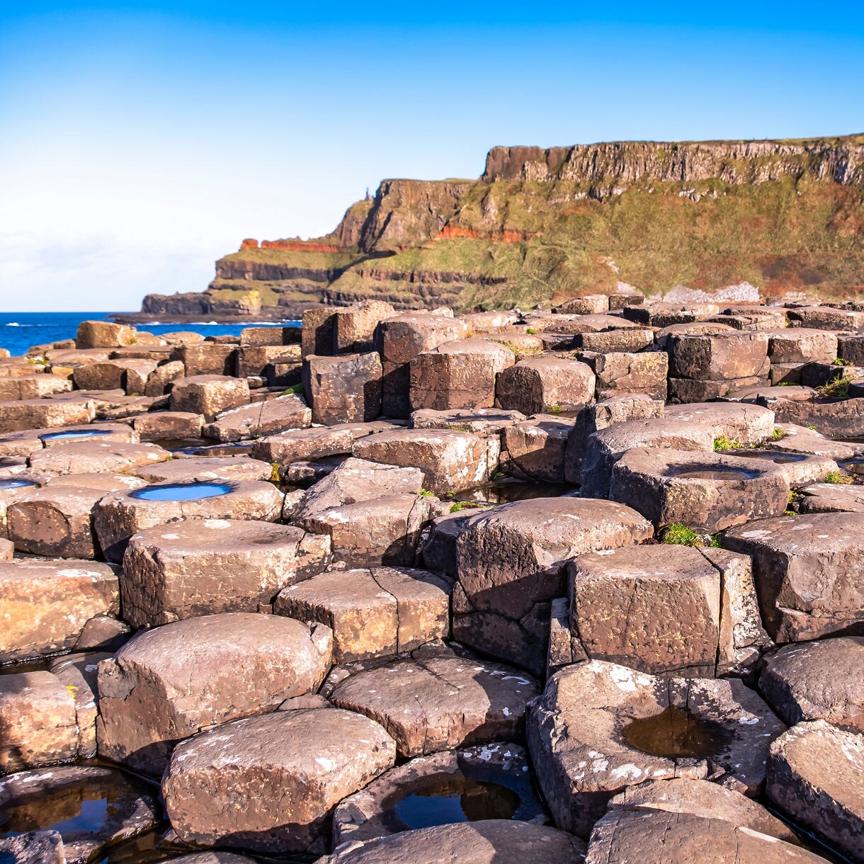 Close-up of basalt columns at the Giant’s Causeway with cliffs and blue sky in the background.