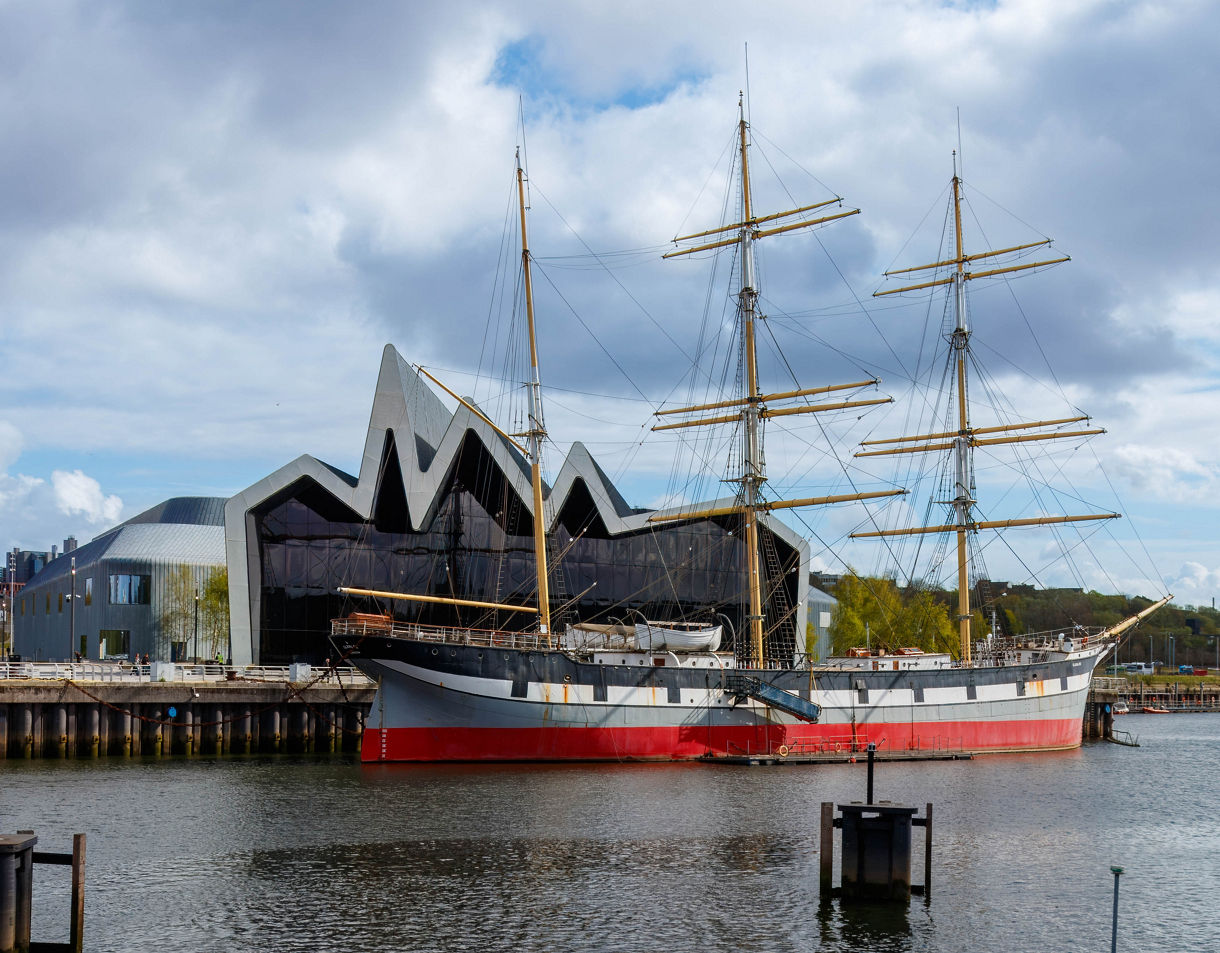 The Tall Ship Glenlee docked in front of the modern, zigzag-roofed Riverside Museum on the River Clyde in Glasgow.