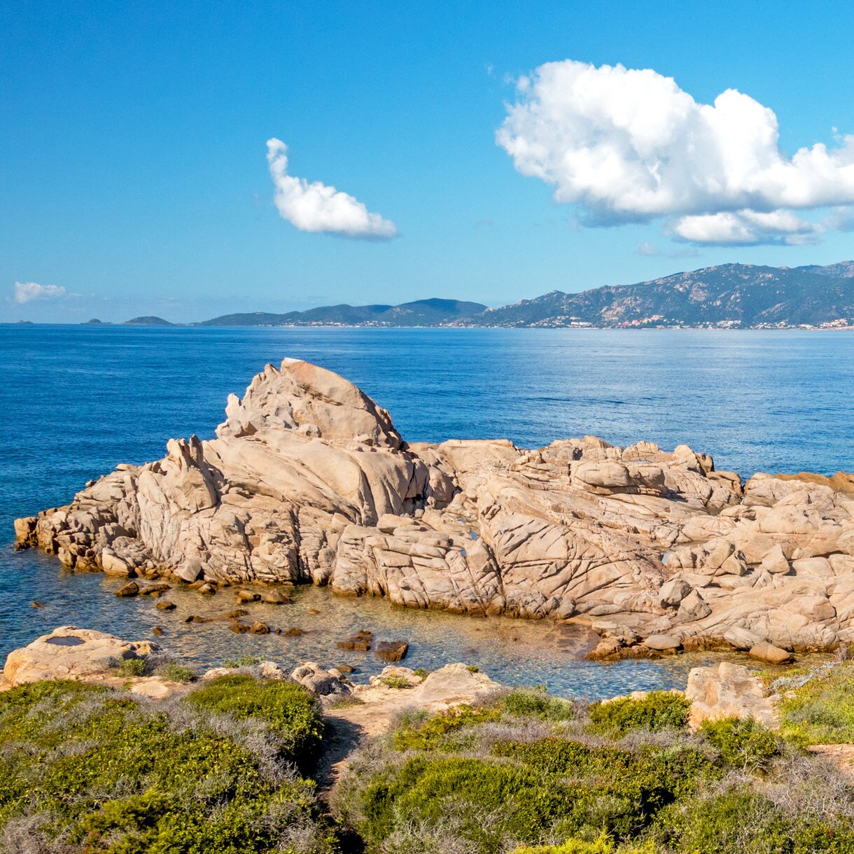 Panoramic view of the Golfe d’Ajaccio in Corsica, featuring rocky coastline, clear blue water and distant mountains under a bright sky.