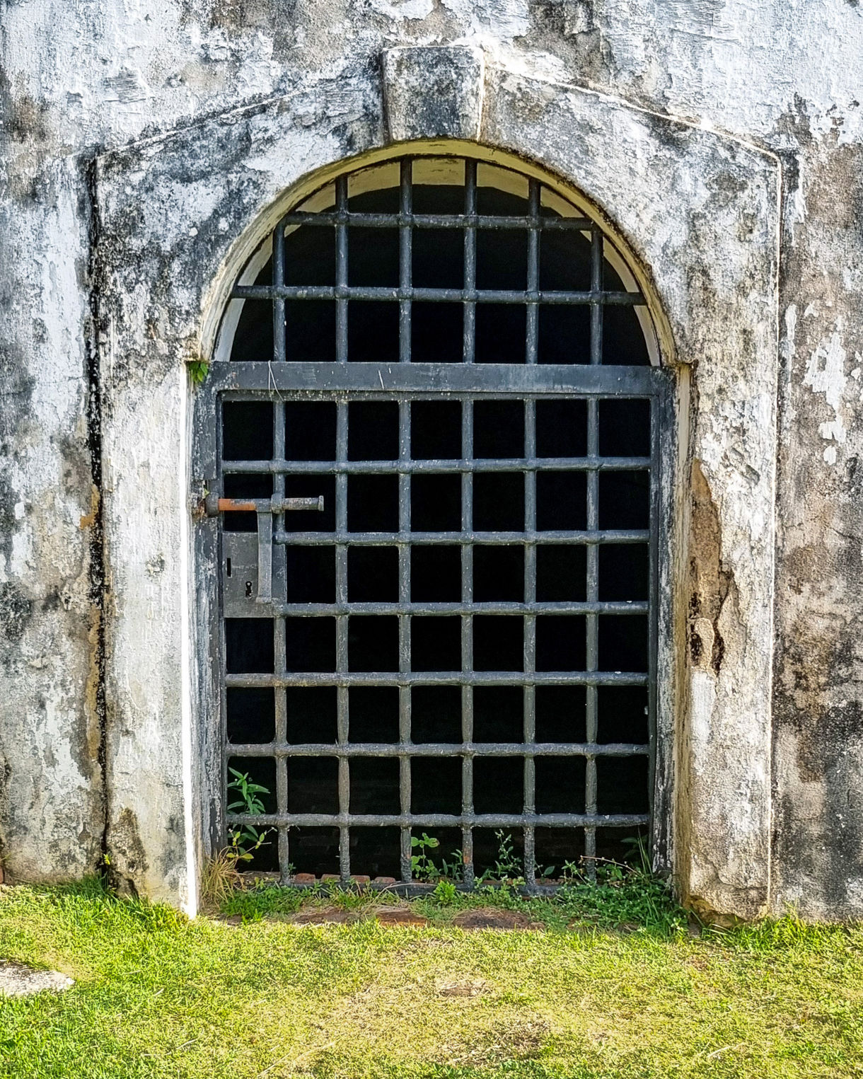 Old stone fortress with a cylindrical lookout tower and sloped green lawn beneath a cloudy sky.