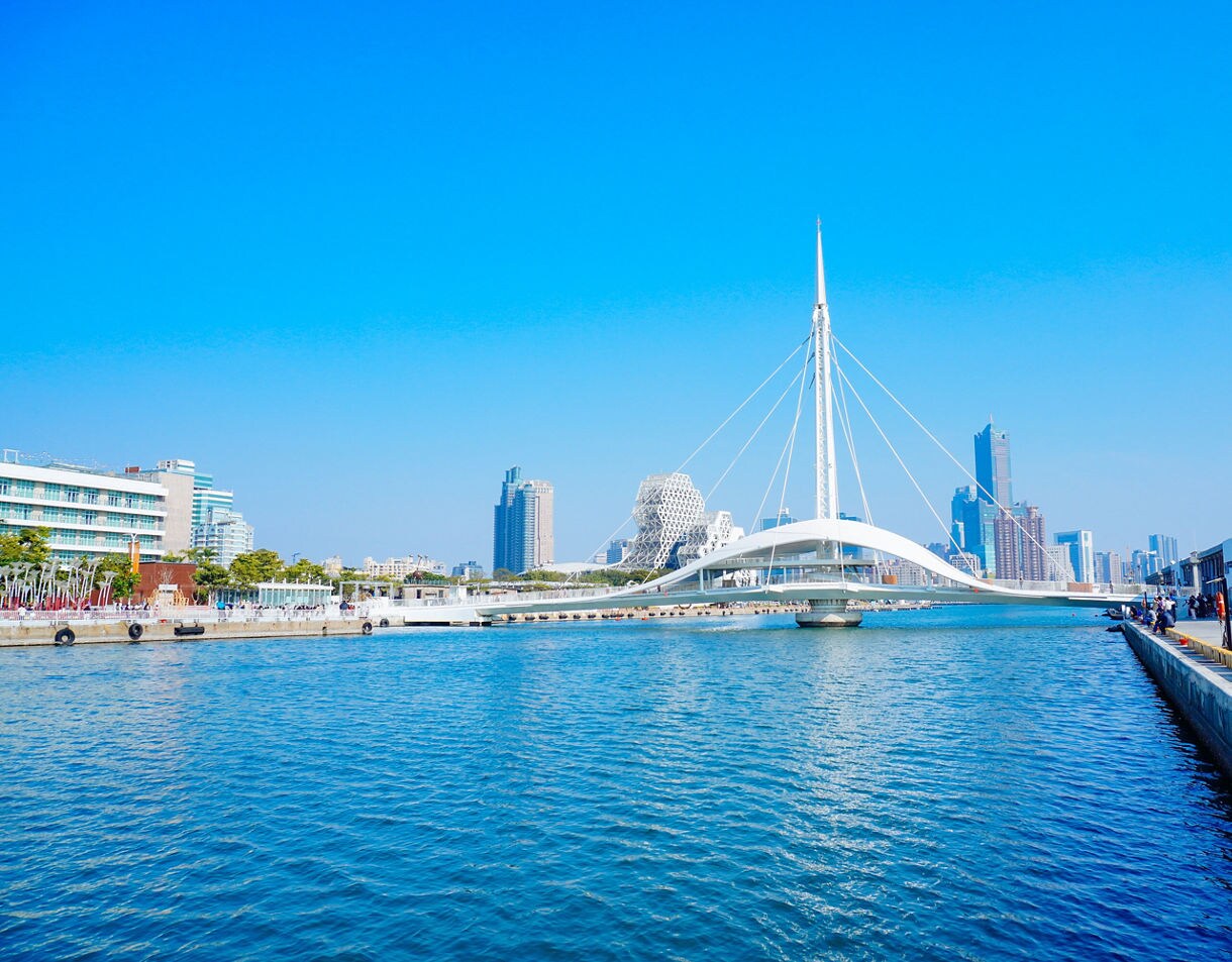  The white, modern Great Harbor Bridge spanning Kaohsiung’s harbor, with blue water below and the city’s skyline rising in the distance under a clear sky.
