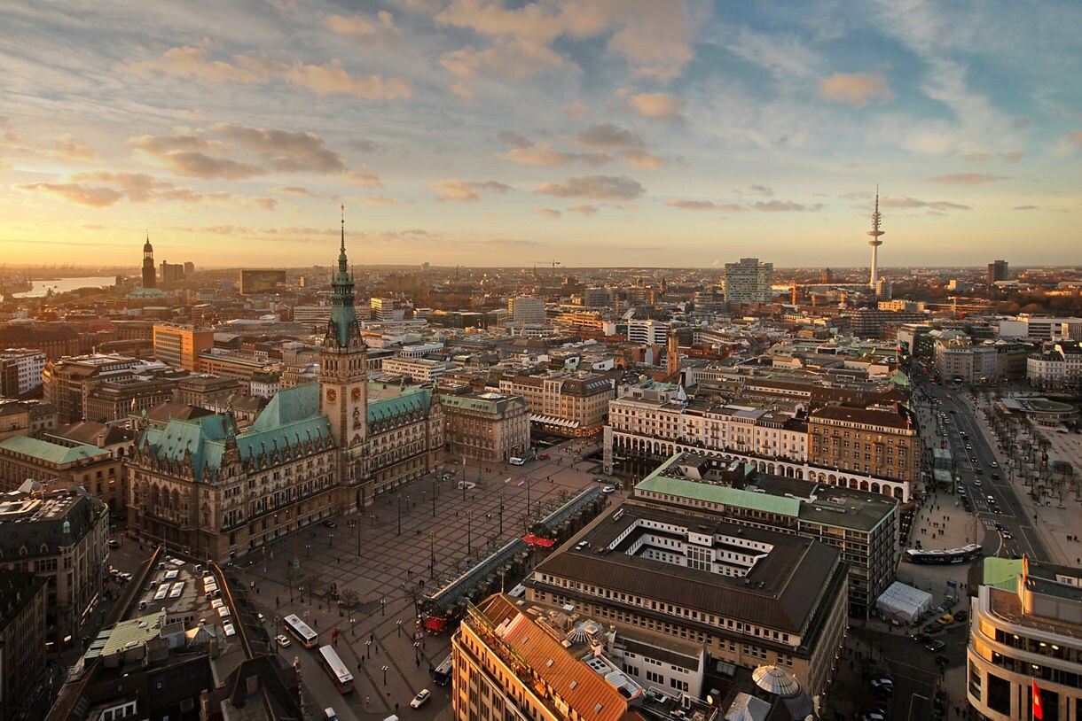 Aerial view of Hamburg’s City Hall with its green copper roof, surrounding square and city buildings under a warm sunset sky.