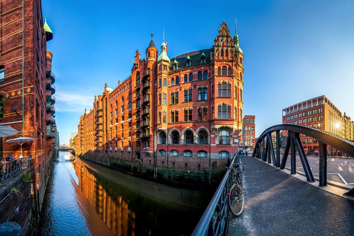 View of Hamburg’s Speicherstadt warehouse district with historic red-brick buildings, arched windows and a canal reflecting the evening light.