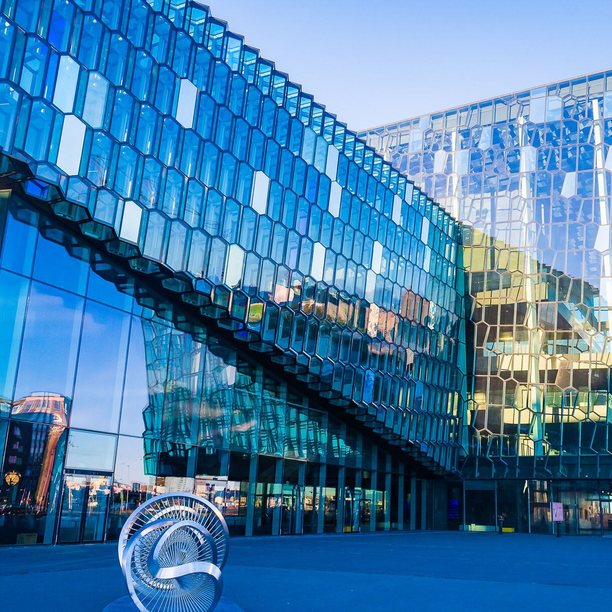 Harpa Concert Hall in Reykjavik, Iceland, with a striking geometric glass exterior reflecting blue skies and surrounding buildings.