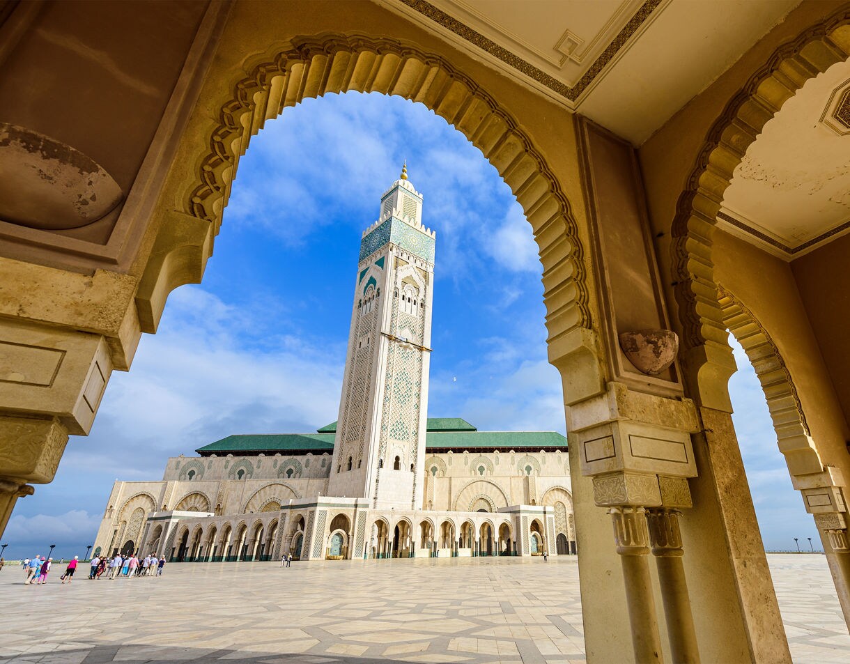 A tall mosque minaret seen through decorative stone archways in a wide open courtyard.