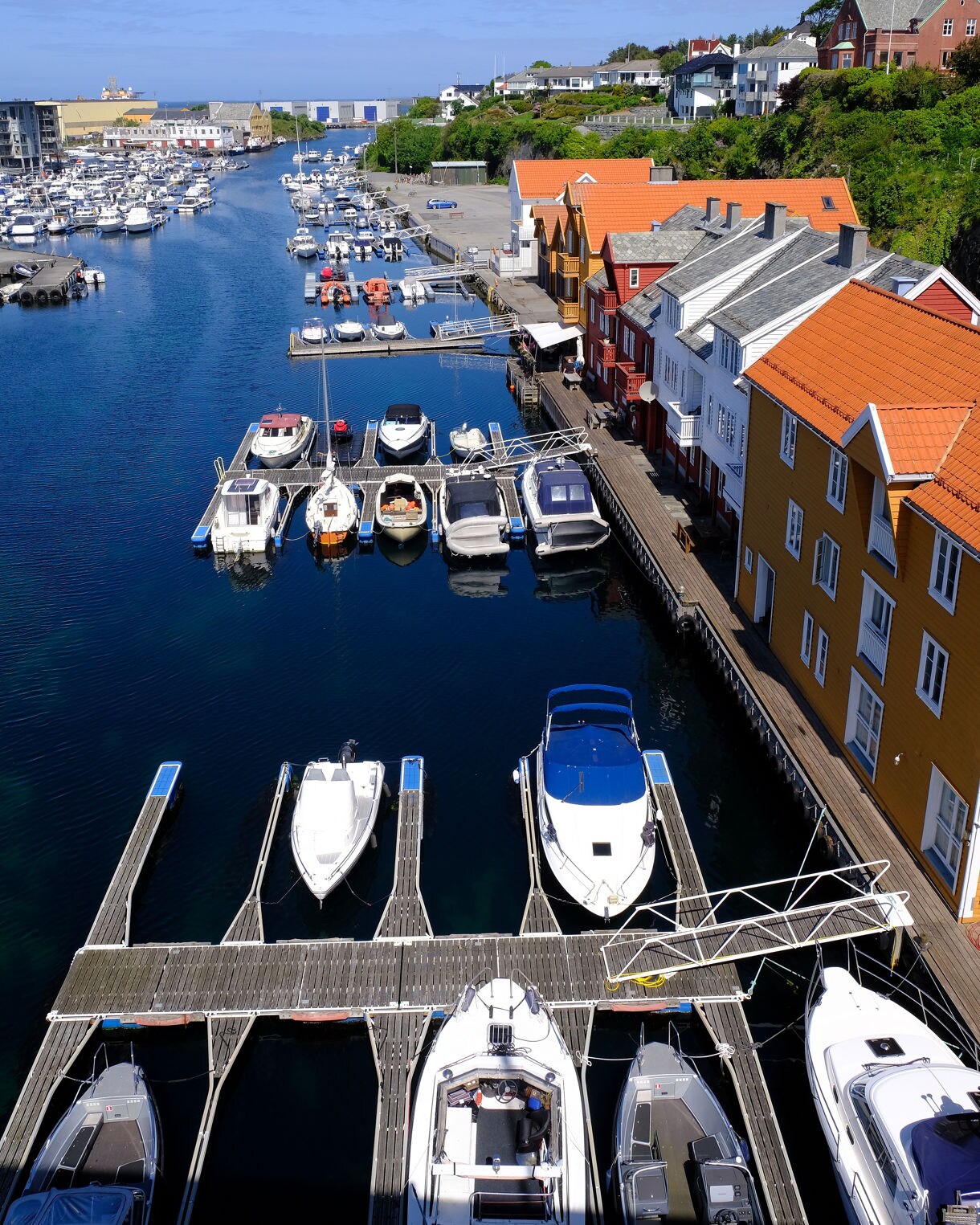 Boats docked in a marina along Haugesund’s waterfront, lined with colorful houses and orange-tiled roofs, leading out to the open sea.