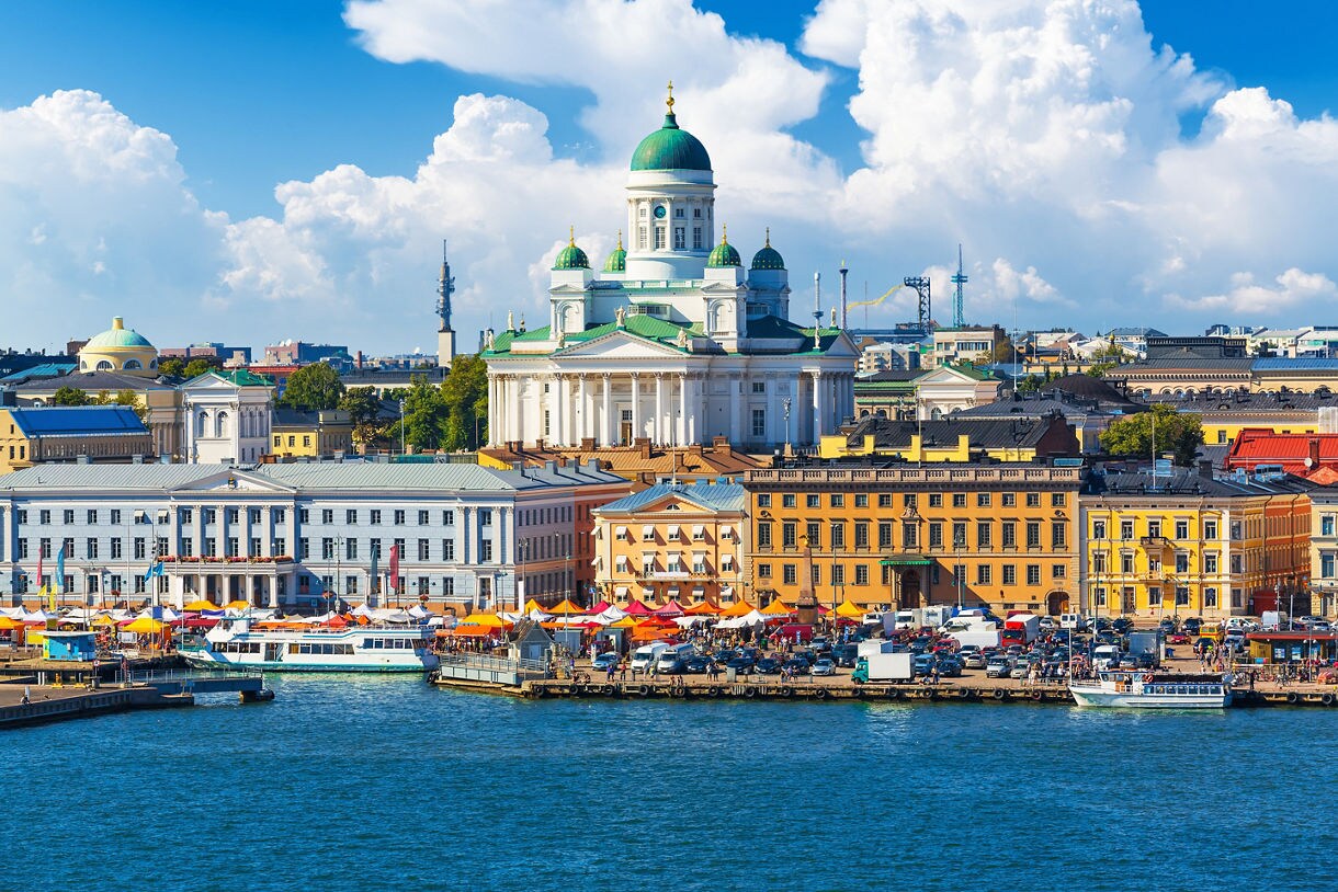Waterfront view of Helsinki with colorful market stalls along the harbor and the white-domed Helsinki Cathedral rising prominently in the background.