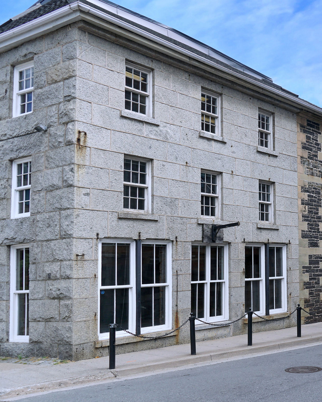 Row of historic stone buildings in Halifax with tall white-framed windows lining a quiet street under a bright blue sky.