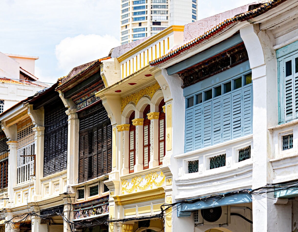 Row of traditional shophouses in George Town, Penang, featuring pastel facades, wooden shutters and ornate details.
