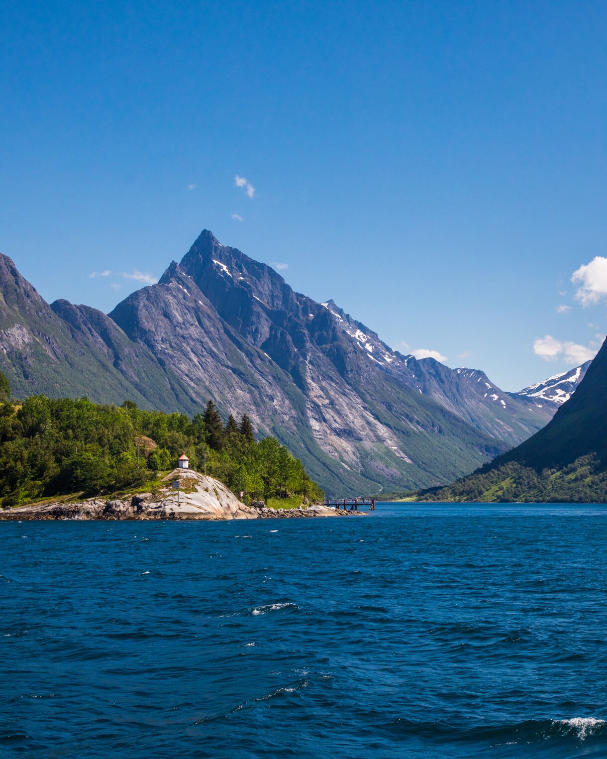 Aerial view of Giske Island with green farmland surrounded by calm blue waters and distant mountain ranges.