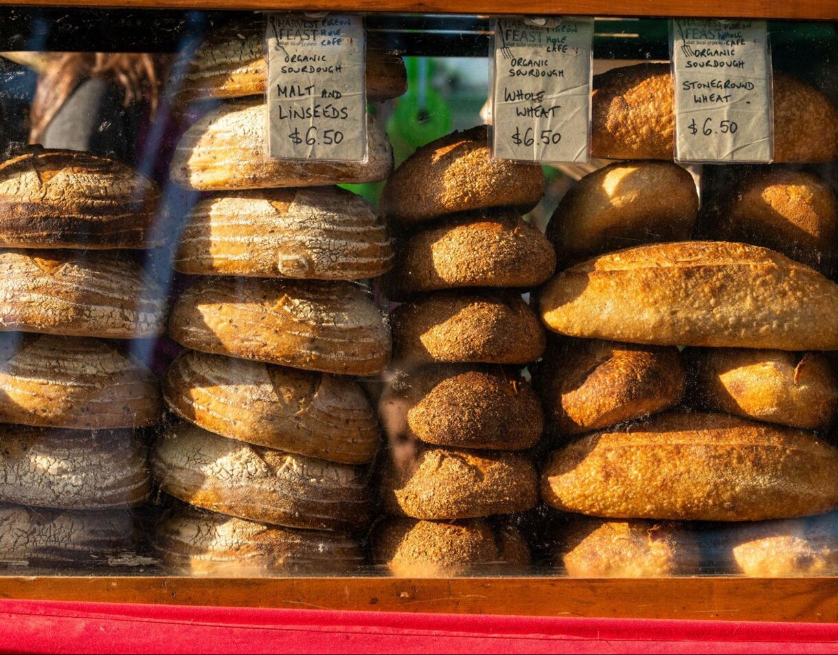 Display case filled with artisan sourdough bread varieties, including whole wheat, stoneground wheat and malt with linseeds, for sale at Salamanca Market in Hobart.