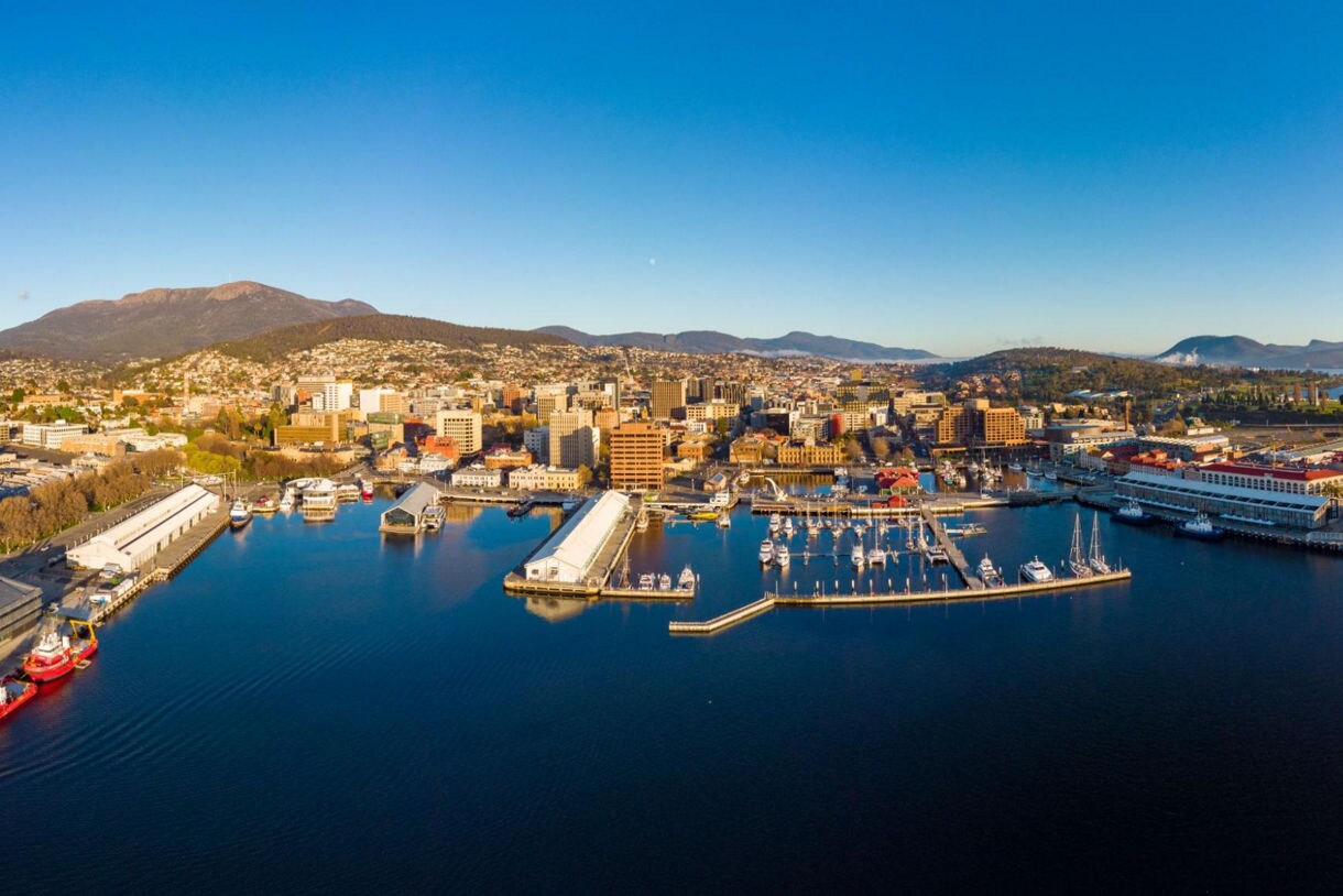 Aerial view of Hobart, Tasmania, showing the harbor filled with boats, warehouses and city buildings with Mount Wellington in the background.