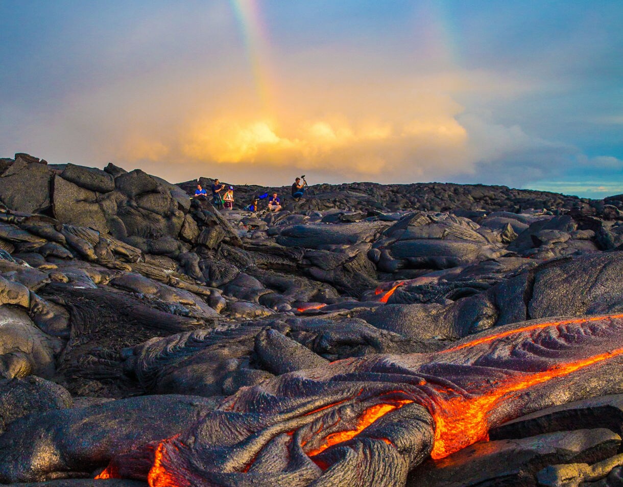 Bright orange lava seeping through cracks in dark, cooled volcanic rock on the Big Island.